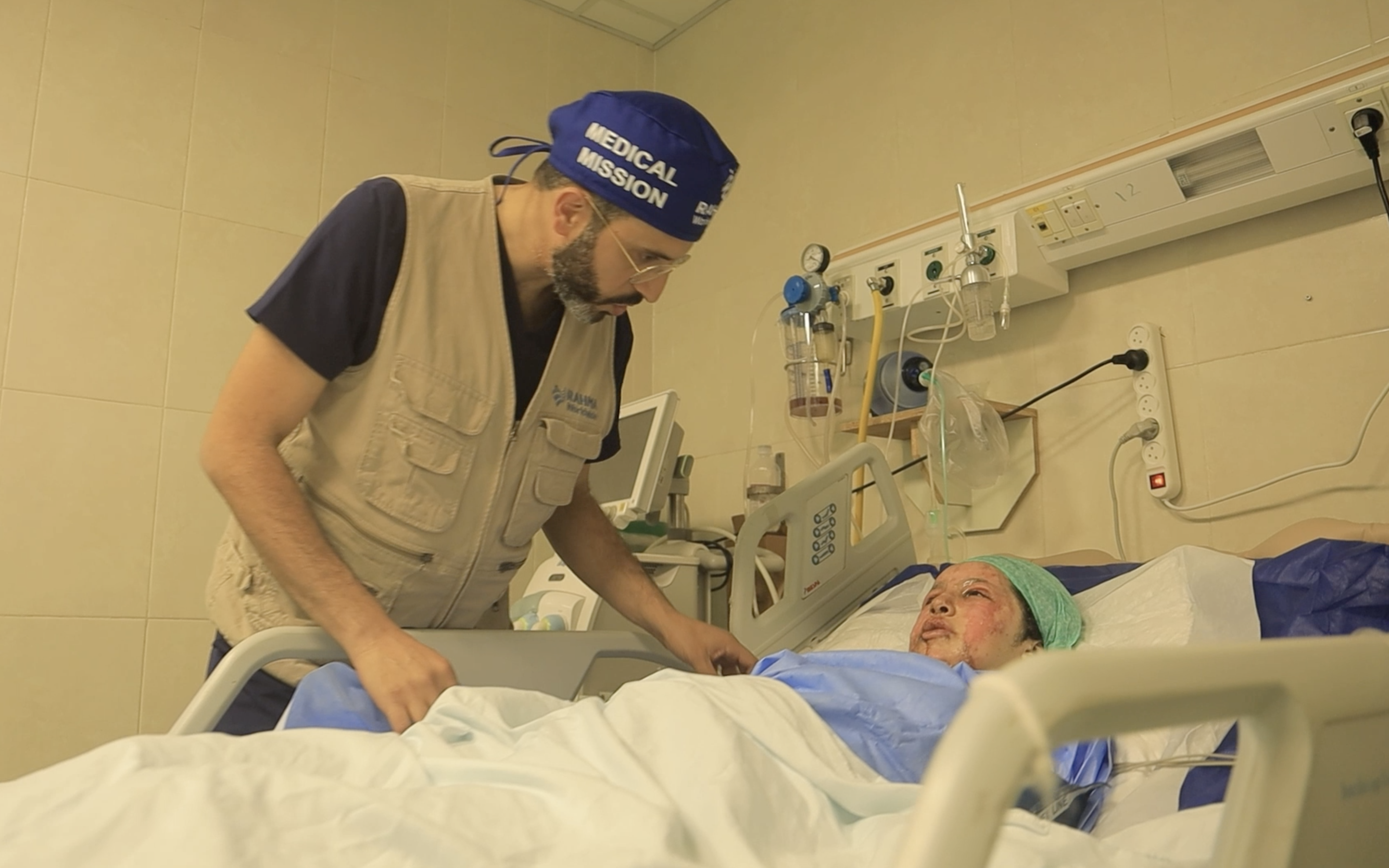 Dr Almanaseer reassures a young patient about the burns covering her body and face [Screengrab/Al Jazeera Mubasher]
